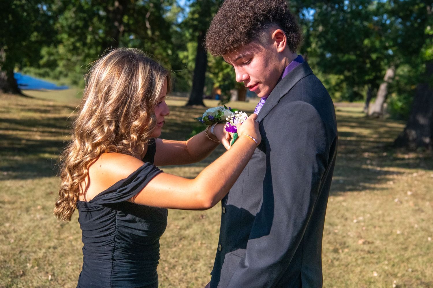 A couple in formal attire shares a romantic dance outdoors in a park setting during a sunny afternoon.