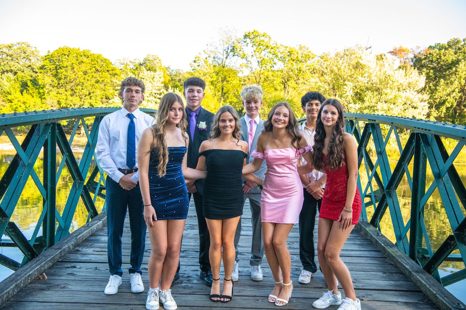 A group poses together on a wooden bridge surrounded by lush greenery on a sunny day.