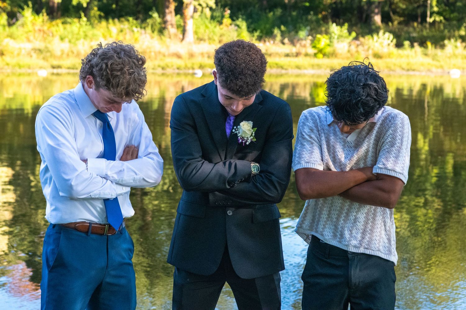 Group of friends in formal attire standing by a lake at sunset during a summer evening celebration.