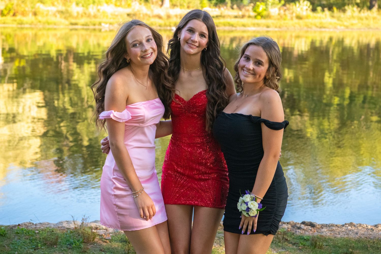 Three people in swimwear posing together by a lakeside on a sunny summer day.