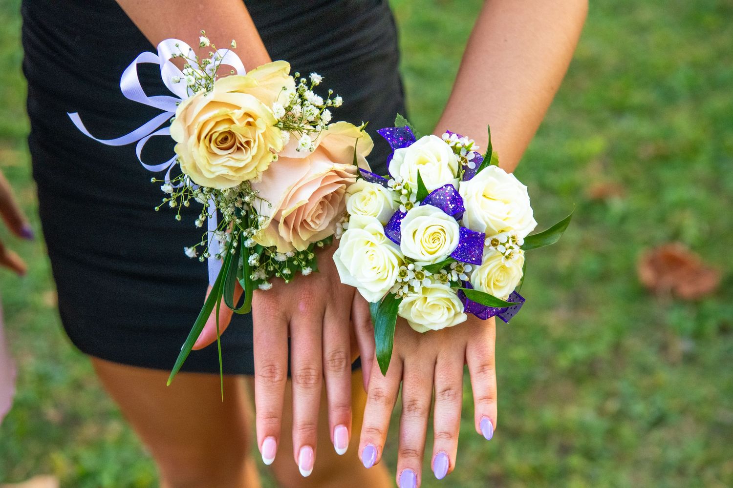 Corsages with yellow and purple flowers are displayed on wrists with formal attire.
