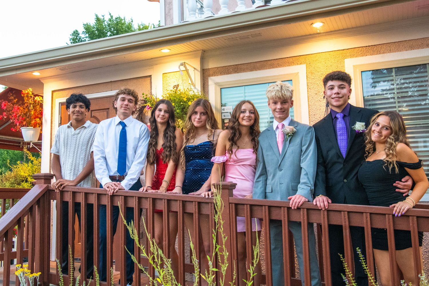 A group of formally dressed people stand on a wooden deck for a special occasion gathering.