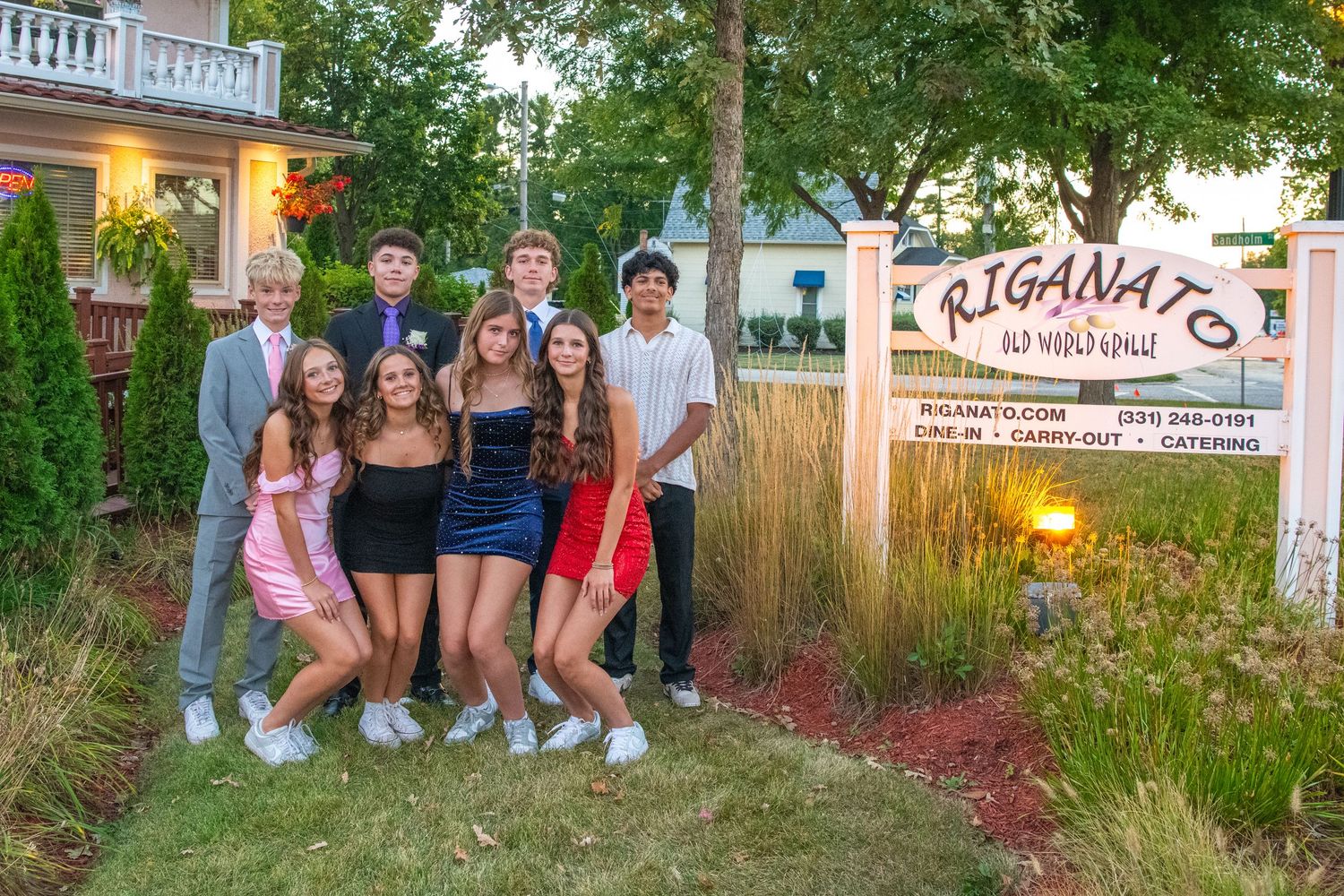 Group photo of friends gathered outside a house with trees and landscaping in the background.