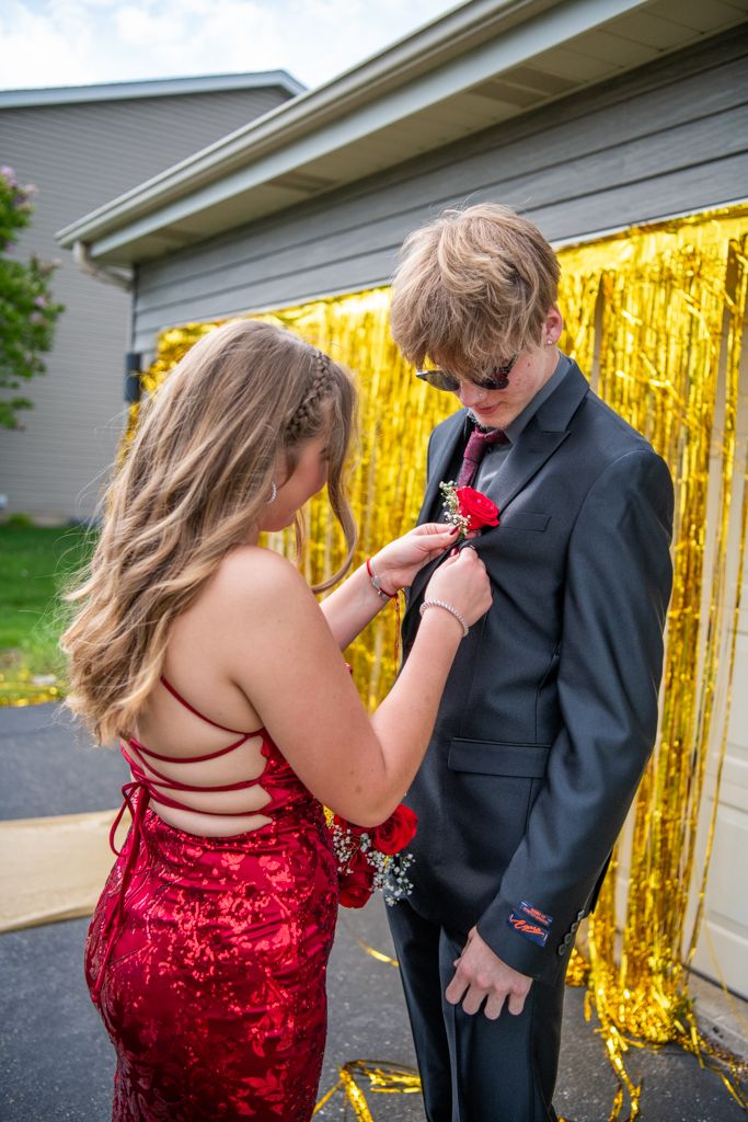 Couple in formal wear posing against a gold tinsel backdrop during a special occasion.
