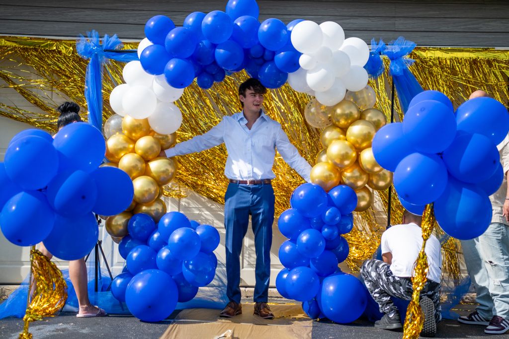 Large balloon arch display featuring blue, white and gold balloons against an outdoor wall.