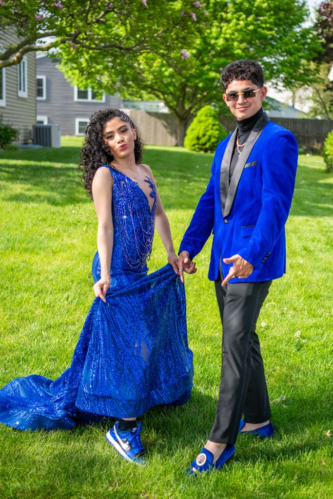 Two people in coordinating blue formal wear pose on green grass during a special event.