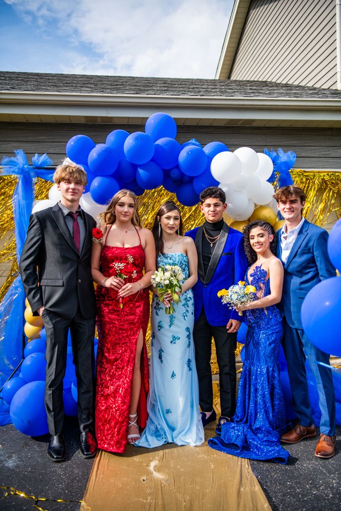 Group photo at formal event with people in sparkly dresses against gold and balloon backdrop.