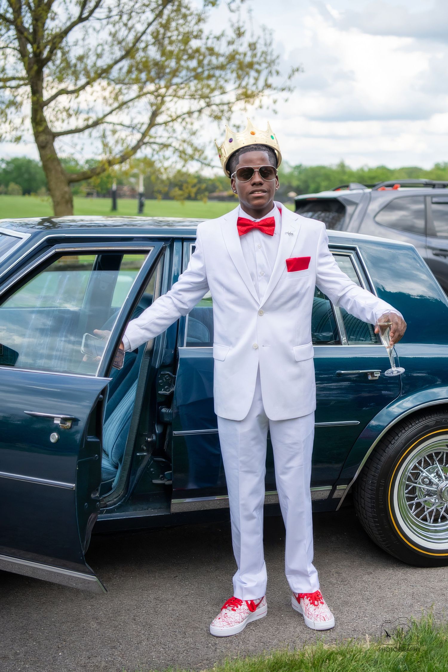 A formal occasion featuring classic black cars and someone in a crisp white suit with red accents.