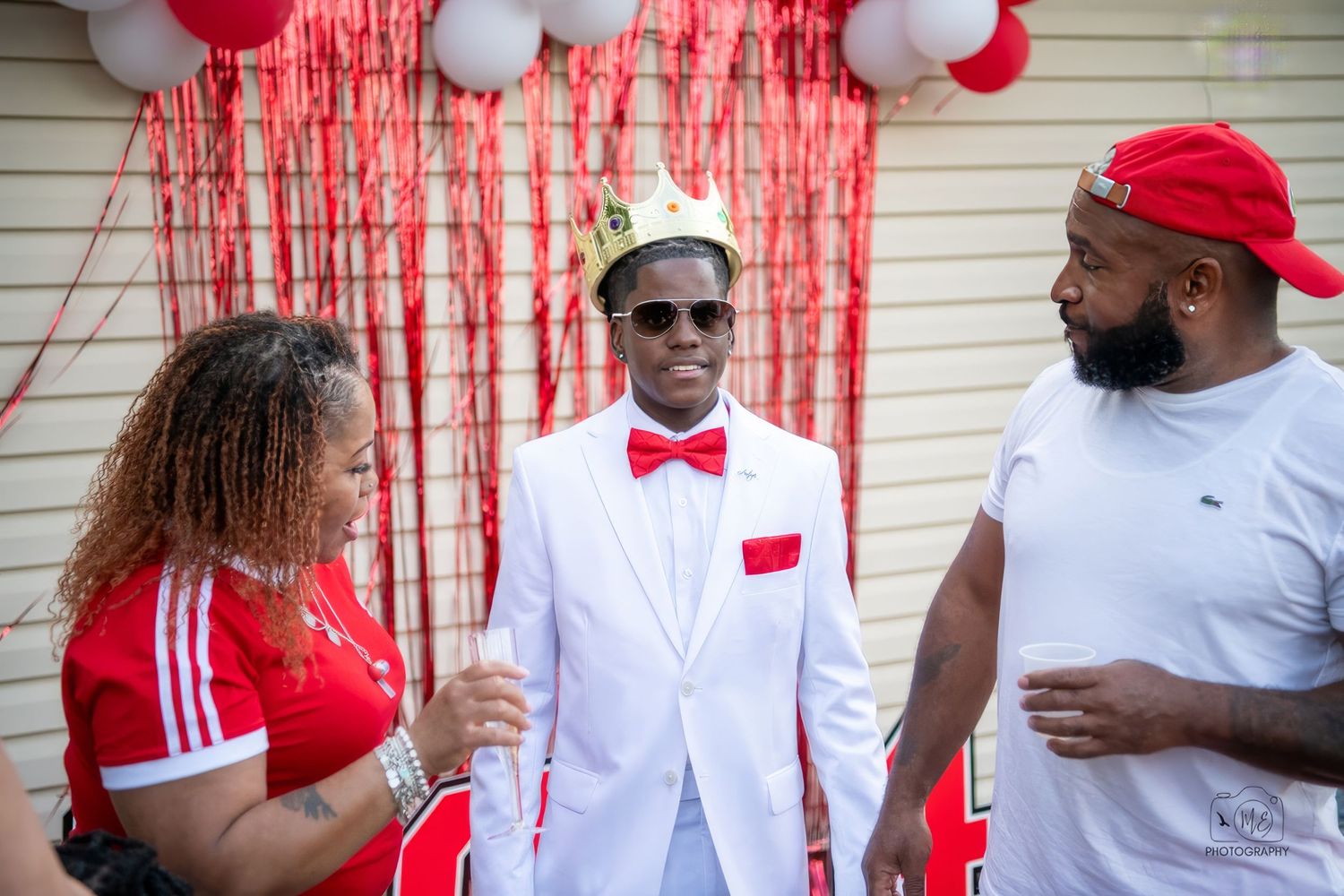 A celebratory scene with red and white balloons against white siding and red dripping decorations.