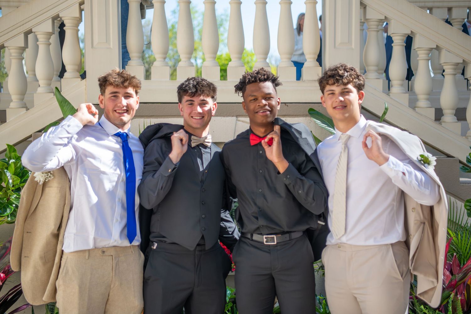 Groomsmen in suits line up against an ornate white balustrade for a formal photo.