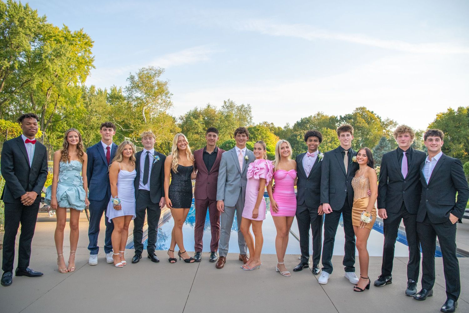 Large wedding party lined up outdoors in formal attire with bridesmaids in pink dresses and groomsmen in dark suits.