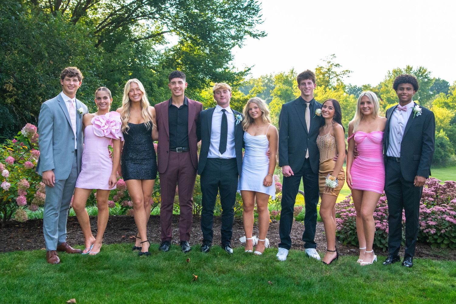 Large group photo of formally dressed attendees posing outdoors on grass at a special event.