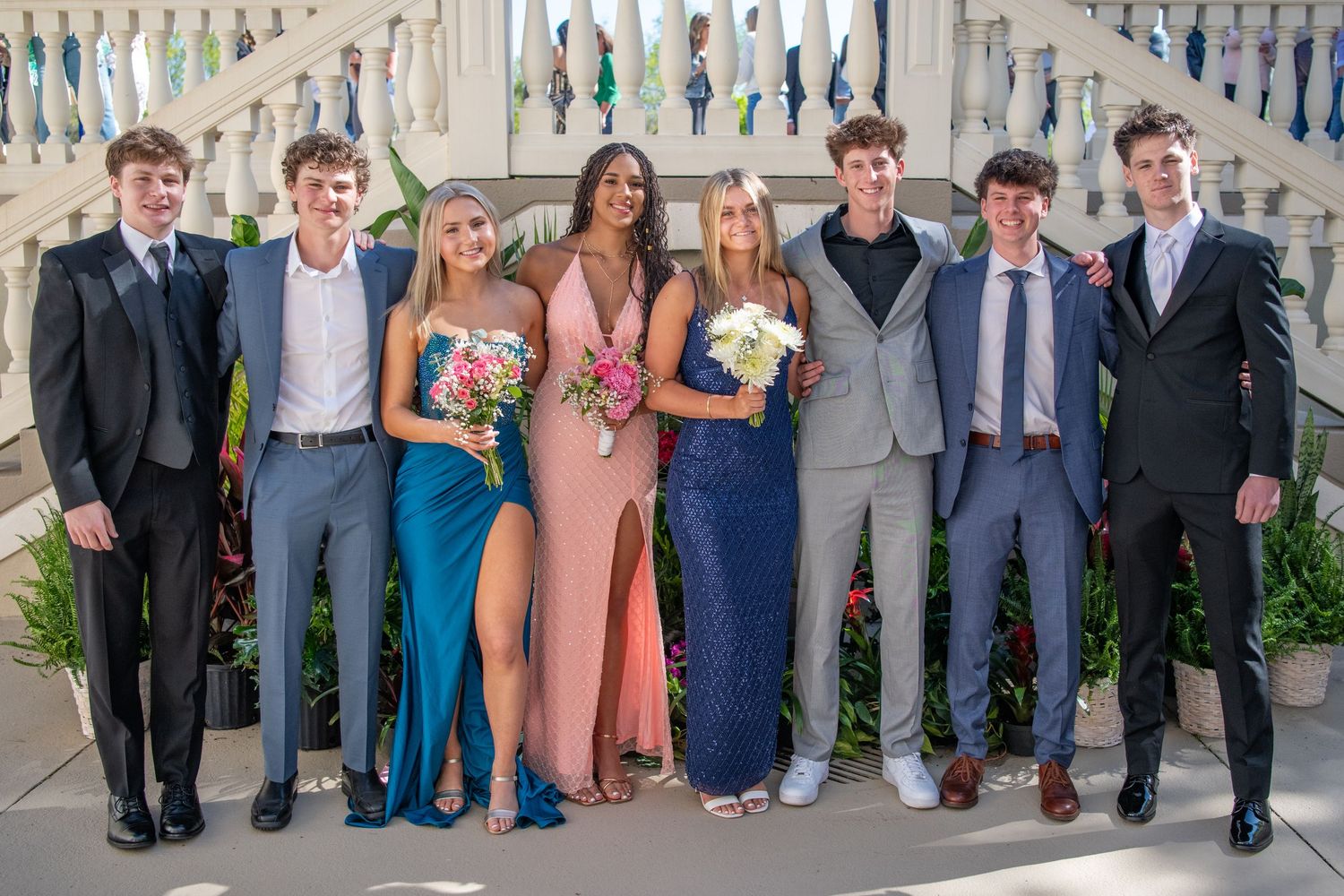 Wedding party members pose together in formal attire against classic white architecture.
