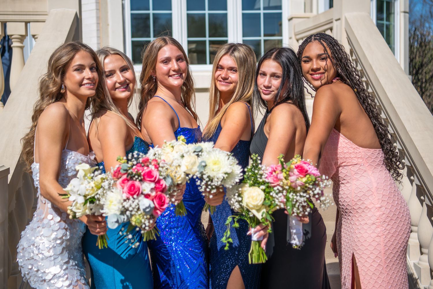 Prom ready in elegant formal dresses holding colorful handmade bouquets.