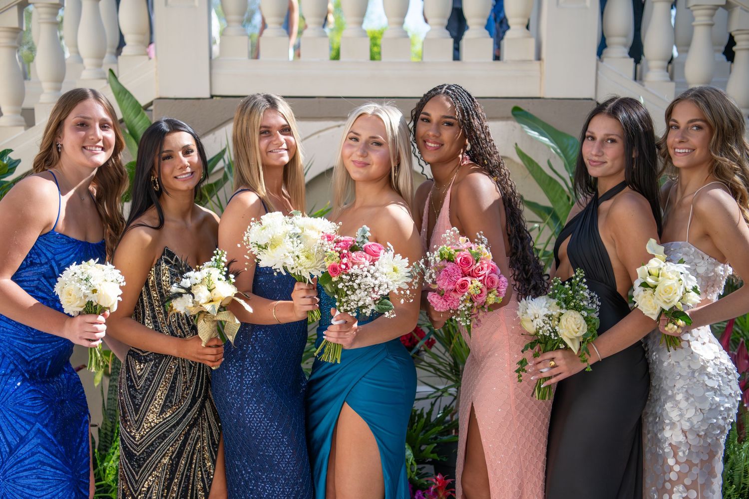 Bridesmaids in coordinated blue and pink dresses hold bouquets while posing together.