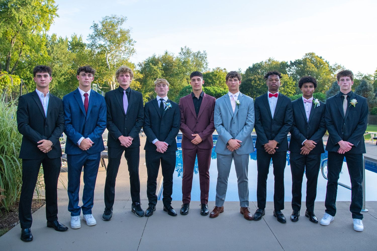 A line of people in formal suits and ties stand together for a group photo outdoors.