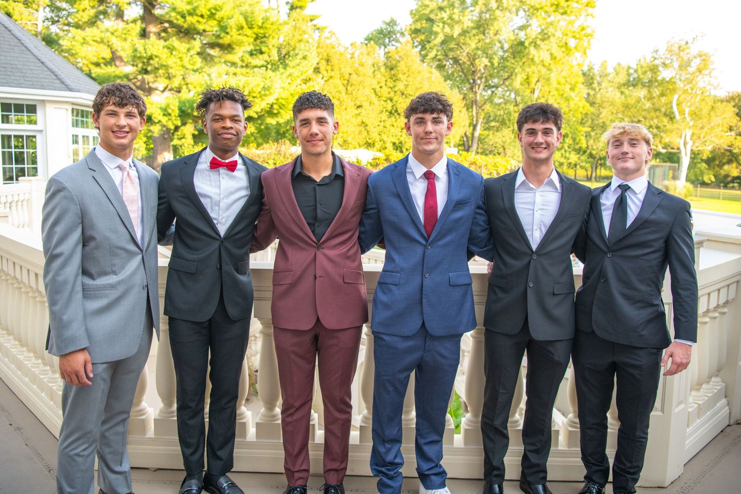 A group of friends in suits and formal attire pose together on steps for a special occasion photo.