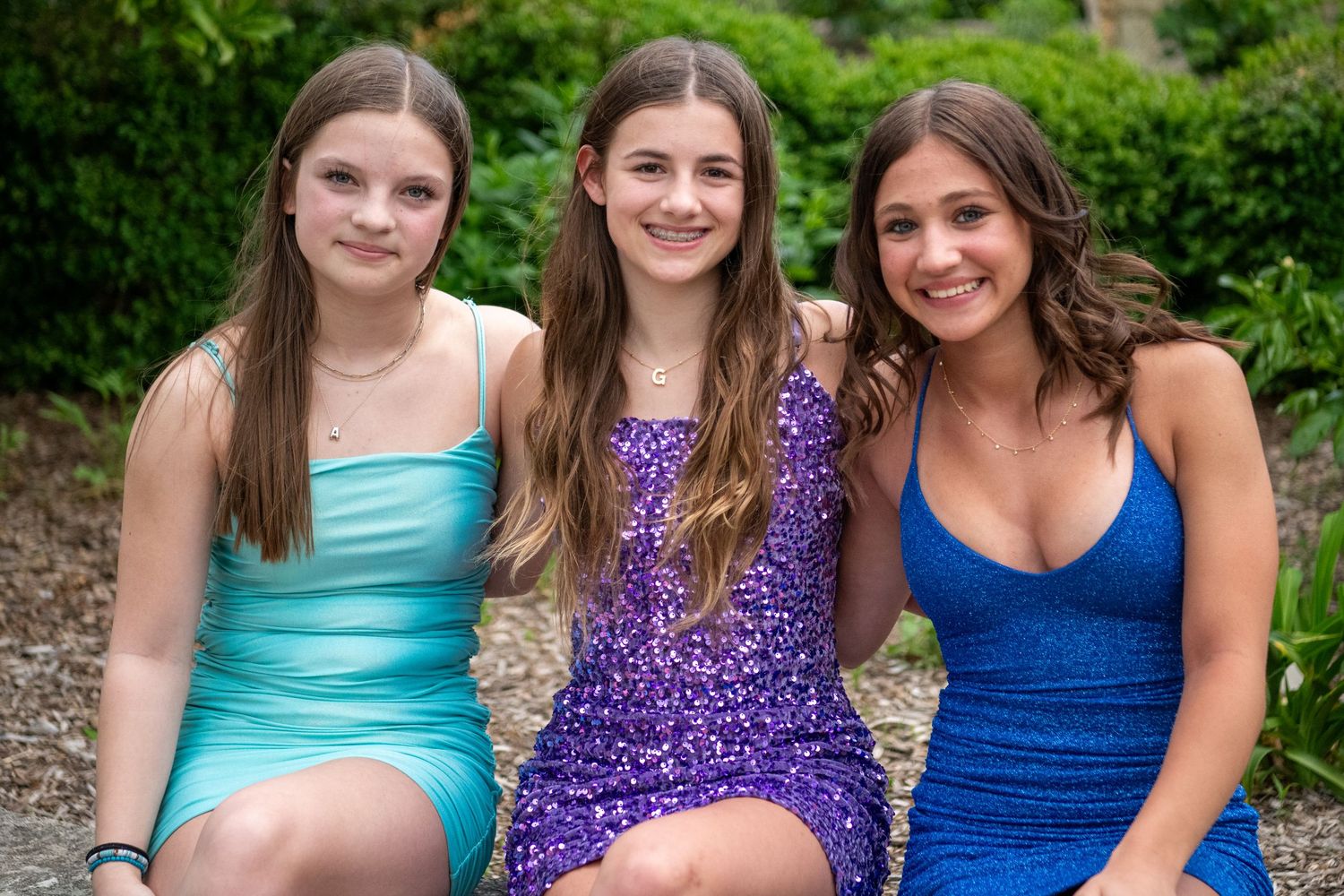 Three friends in sparkling rompers of purple, blue and mint pose together outdoors.