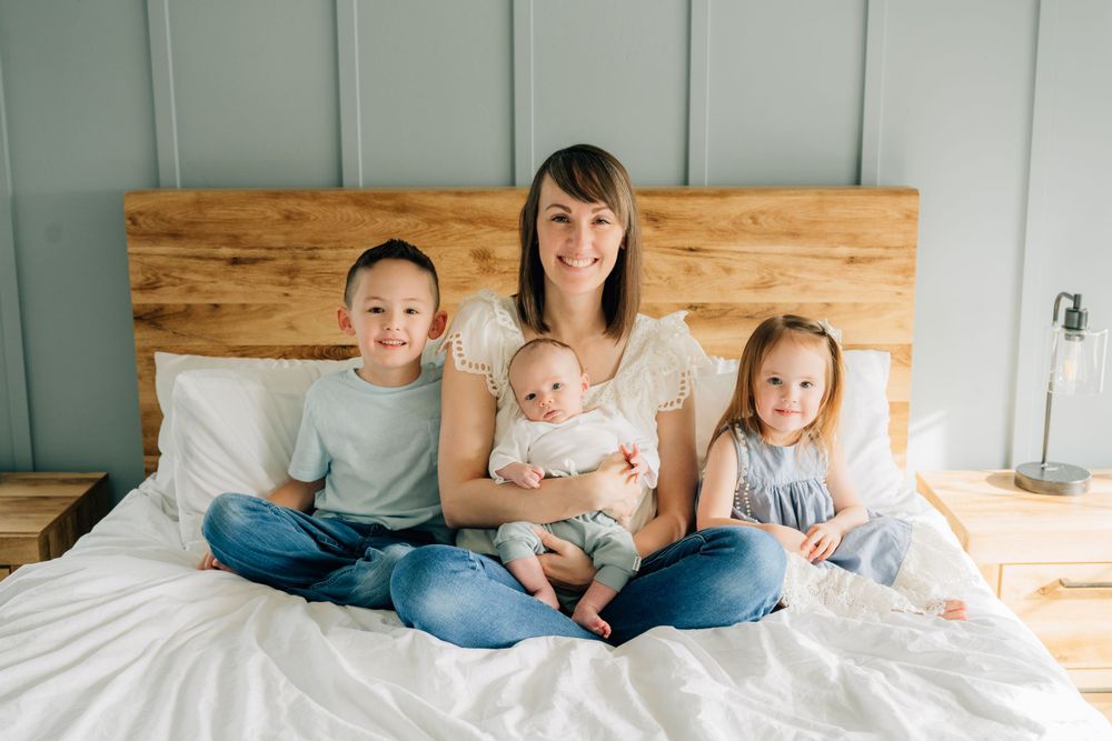 A family sits together on a bed with a rustic wooden headboard while wearing casual blue and white clothing.