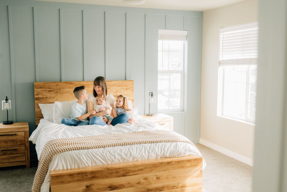 Family relaxing together on rustic wooden bed in bright bedroom with sage green accent wall and natural lighting.