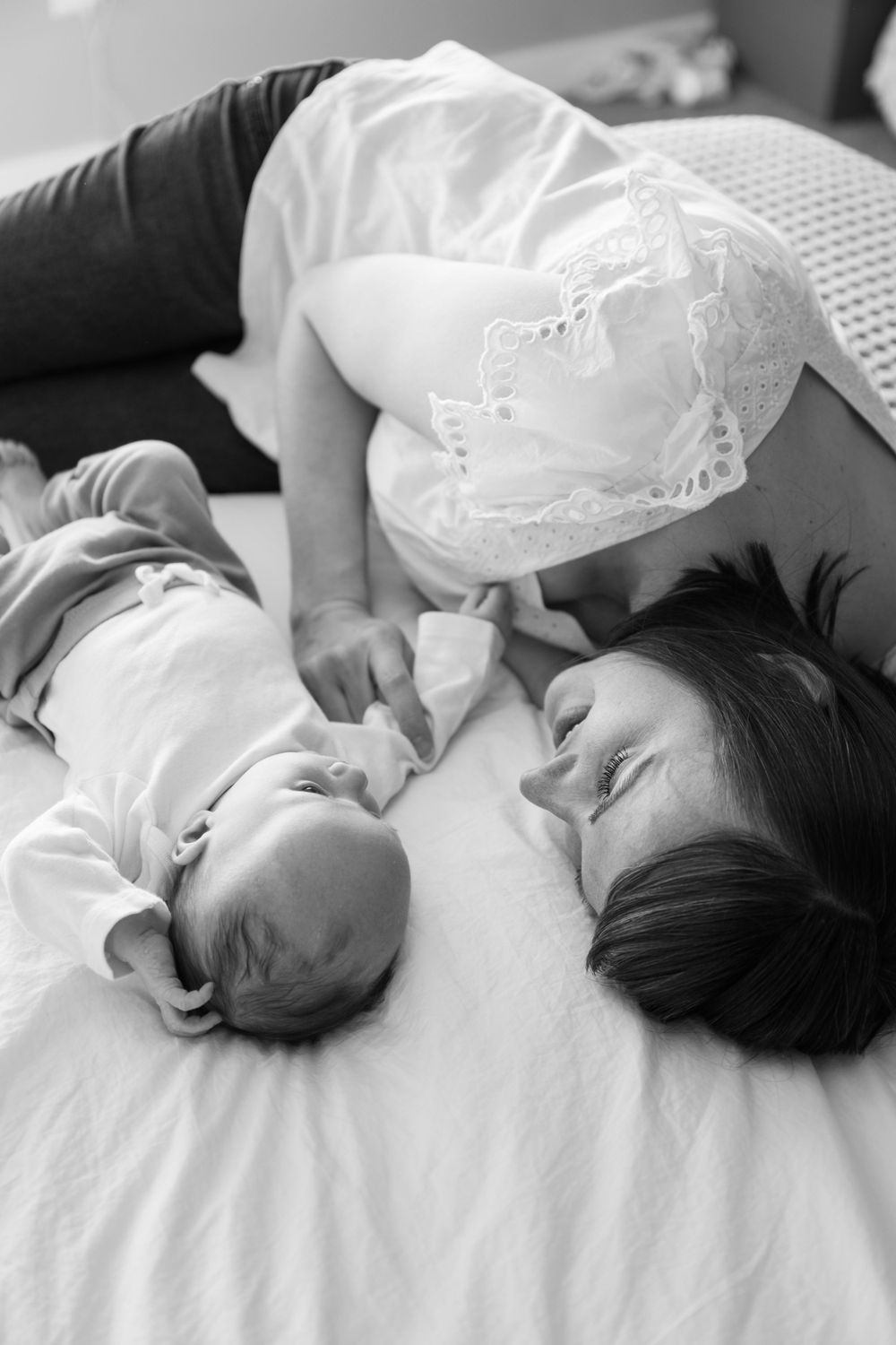 A tender black and white photograph showing a mother and baby lying together on white bedding.