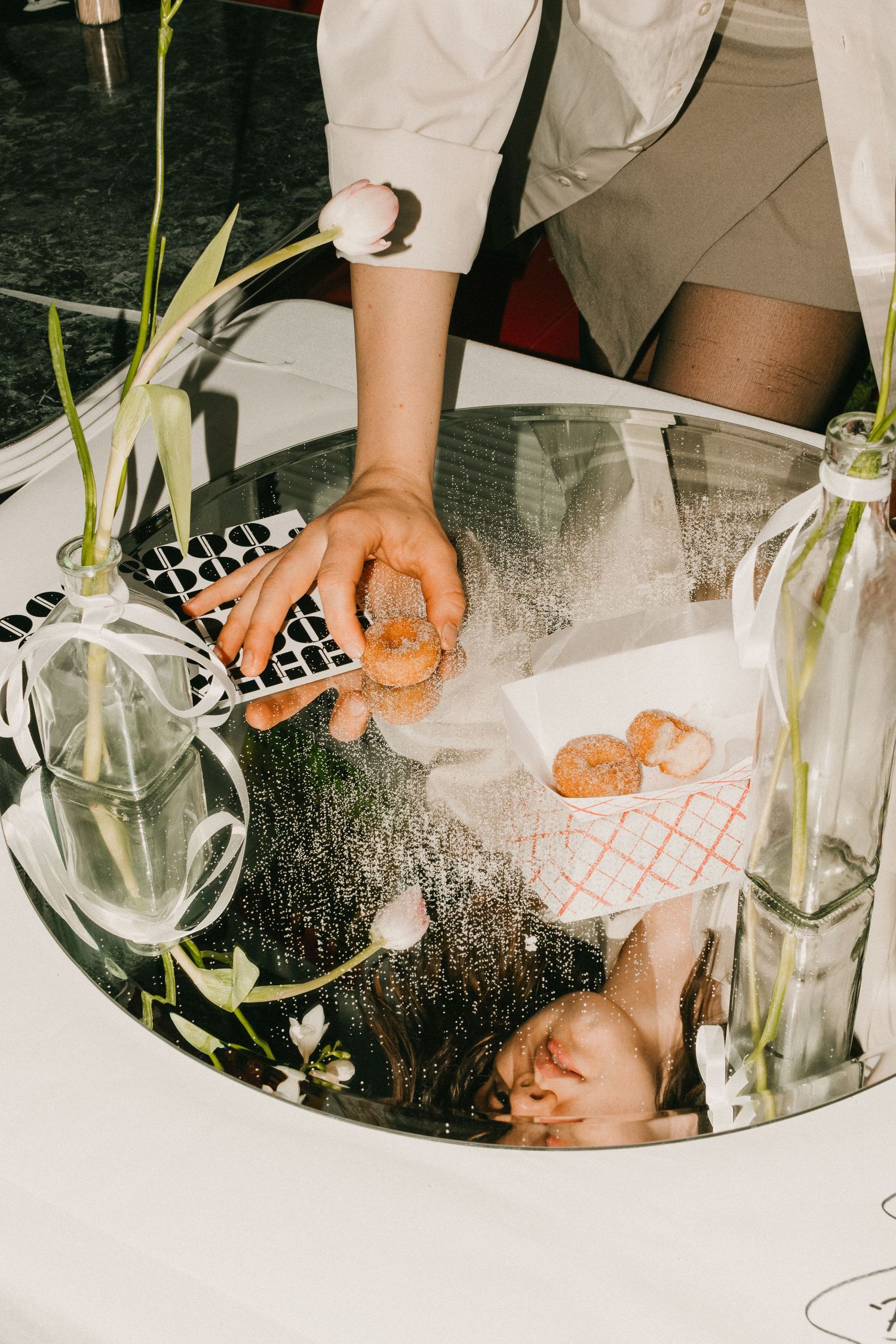 Hands arranging items on a reflective surface with glass vases and floral decorations.