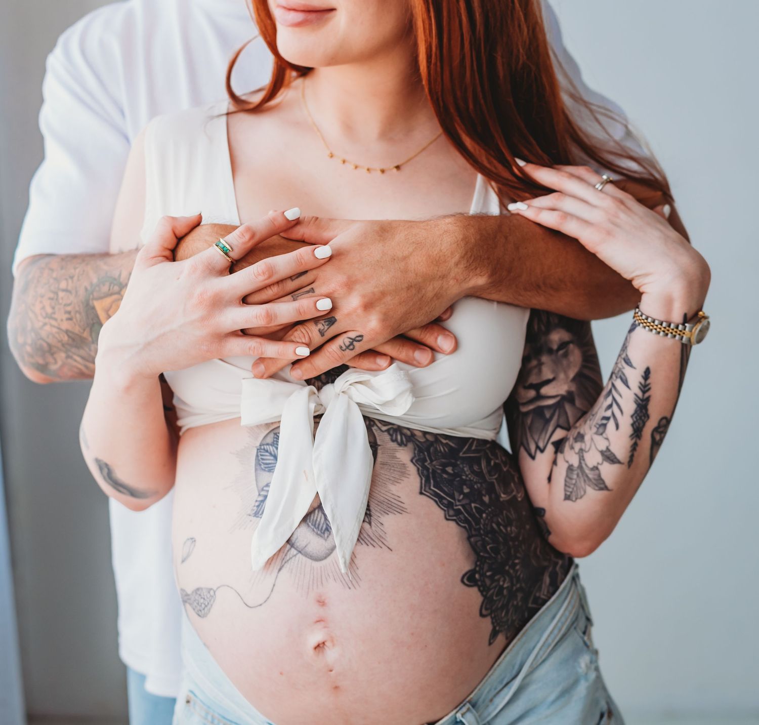 Pregnant woman in dark lace gown posing on vintage gold velvet sofa with boho decor.