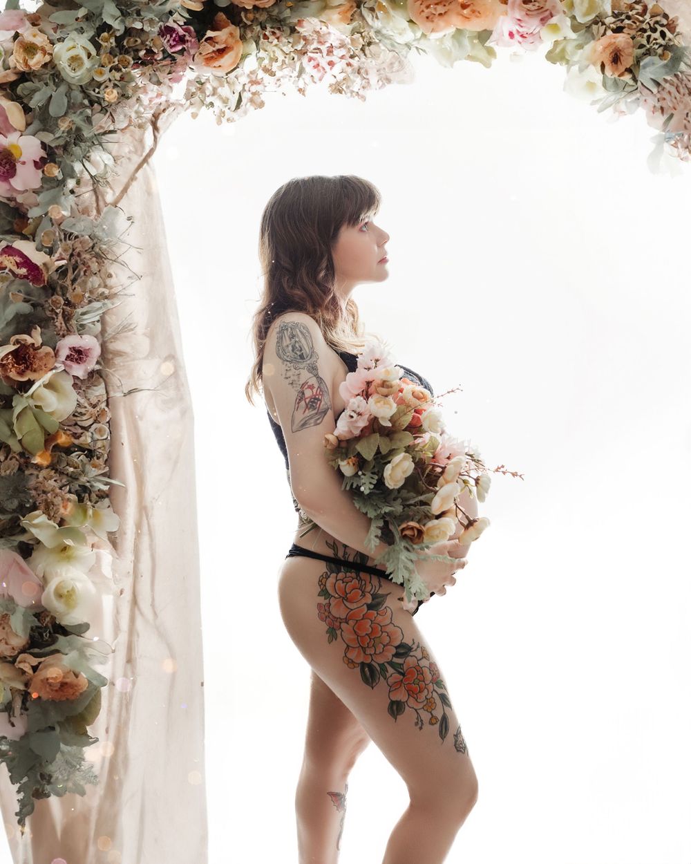 Artistic maternity portrait with floral arrangements and sheer fabric.