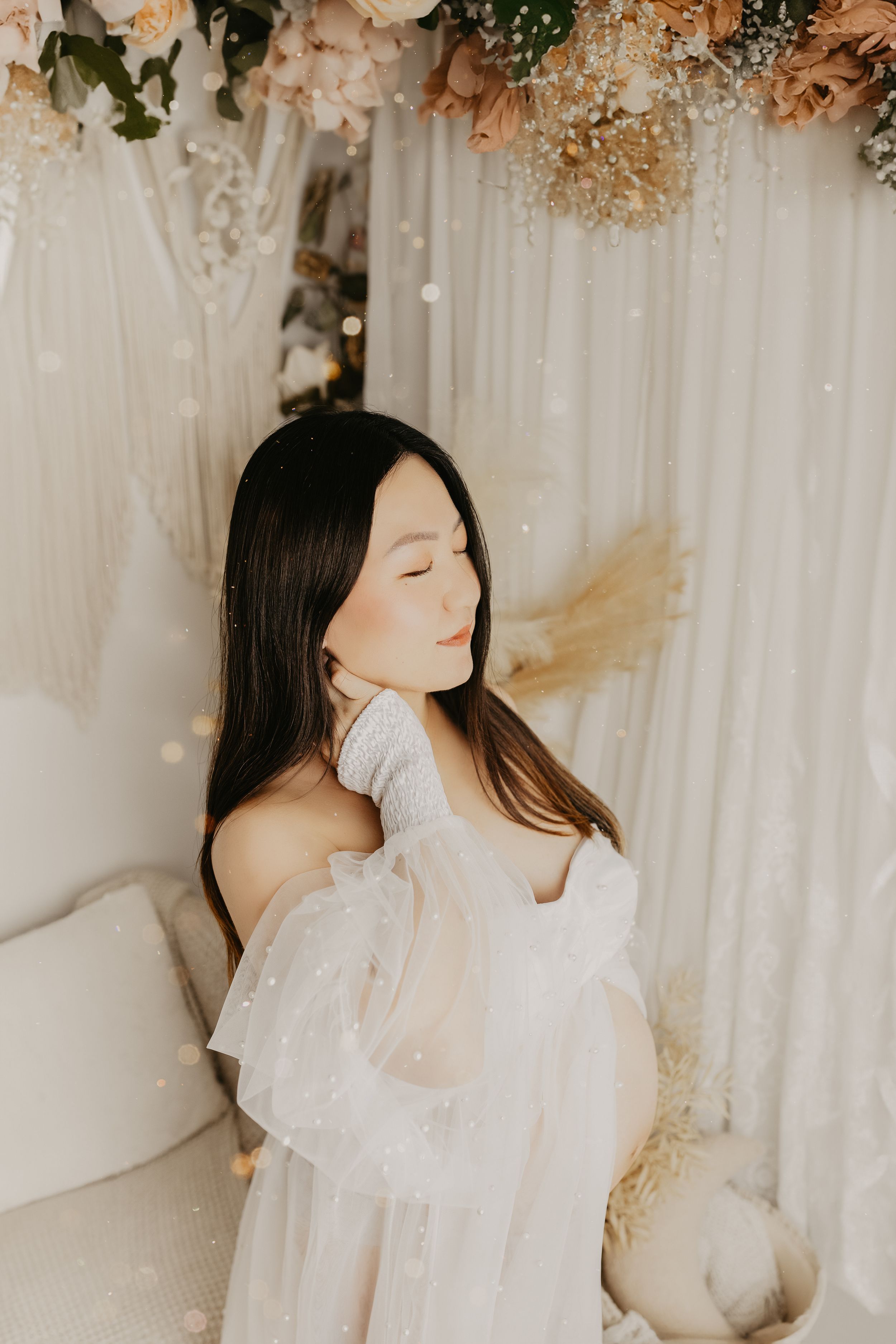 Intimate maternity portraits with soft lighting and floral decorations overhead.