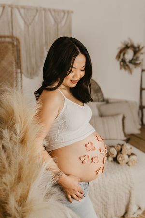 Artistic maternity photo with heart-shaped henna design on belly against neutral backdrop.