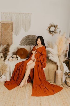 Maternity portrait in flowing rust-colored dress against bohemian backdrop with pampas grass.