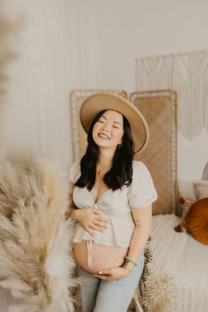 Casual maternity photo with straw hat and white top in boho setting with pampas grass.