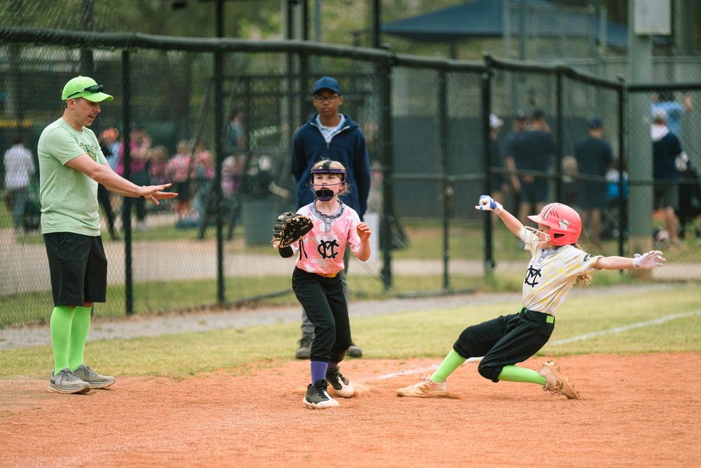 Youth softball players in action during game with sliding play at base.