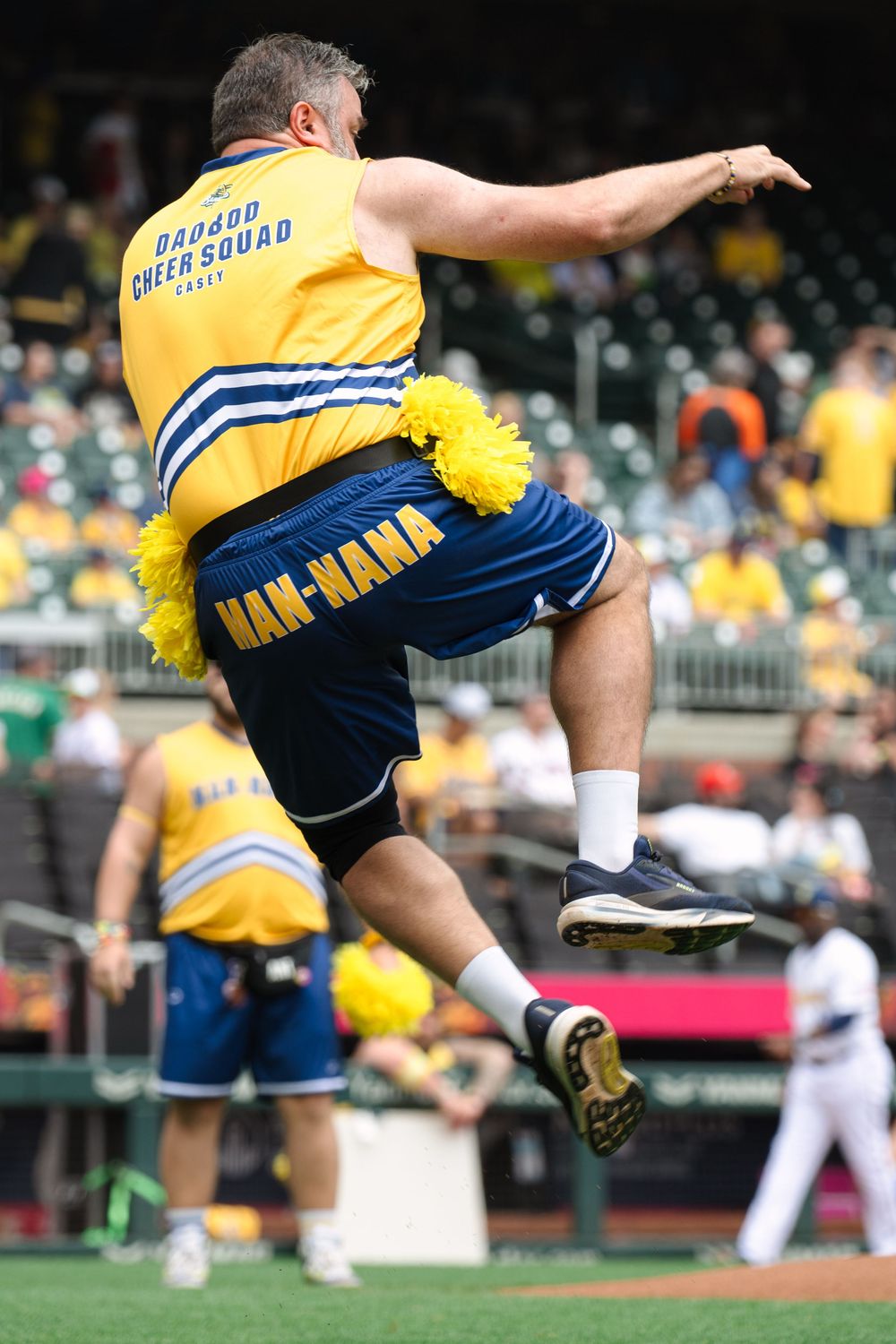 Cheerleader in yellow and blue uniform performs high kick during game.