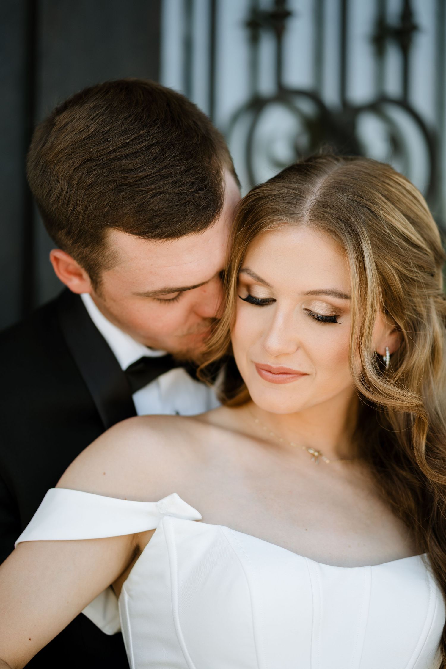 An intimate wedding portrait shows a tender romantic moment between newlyweds in elegant formal attire.