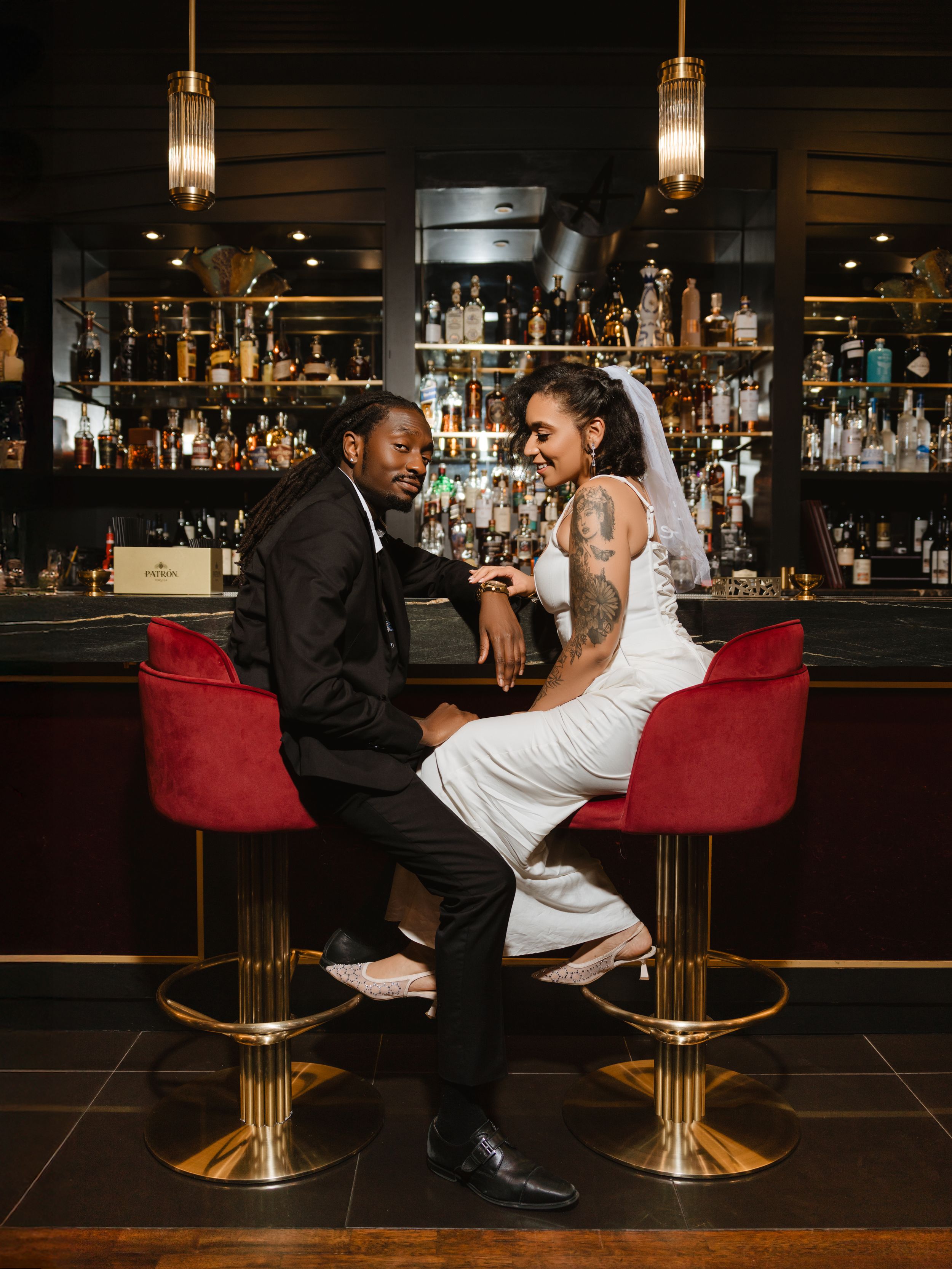 Two people sit at a stylish bar with gold accents and pendant lighting, engaged in animated conversation.