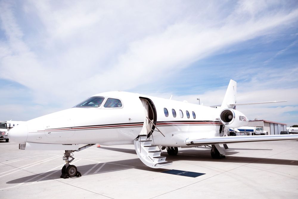 A white private jet parked on tarmac under blue skies with wispy clouds.
