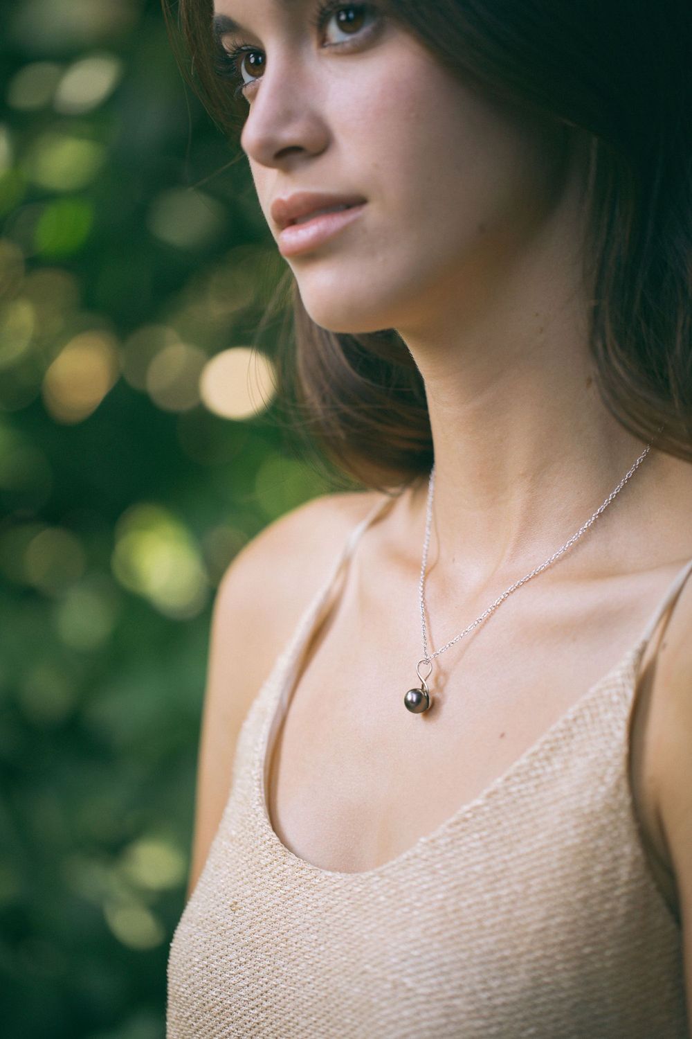 Portrait in beige tank top wearing delicate necklace with soft bokeh background and natural lighting.