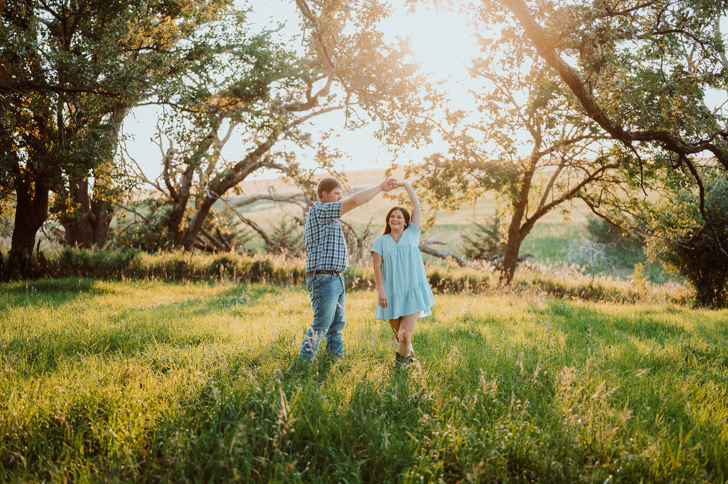 A couple walks hand in hand through a sun-drenched meadow at golden hour.