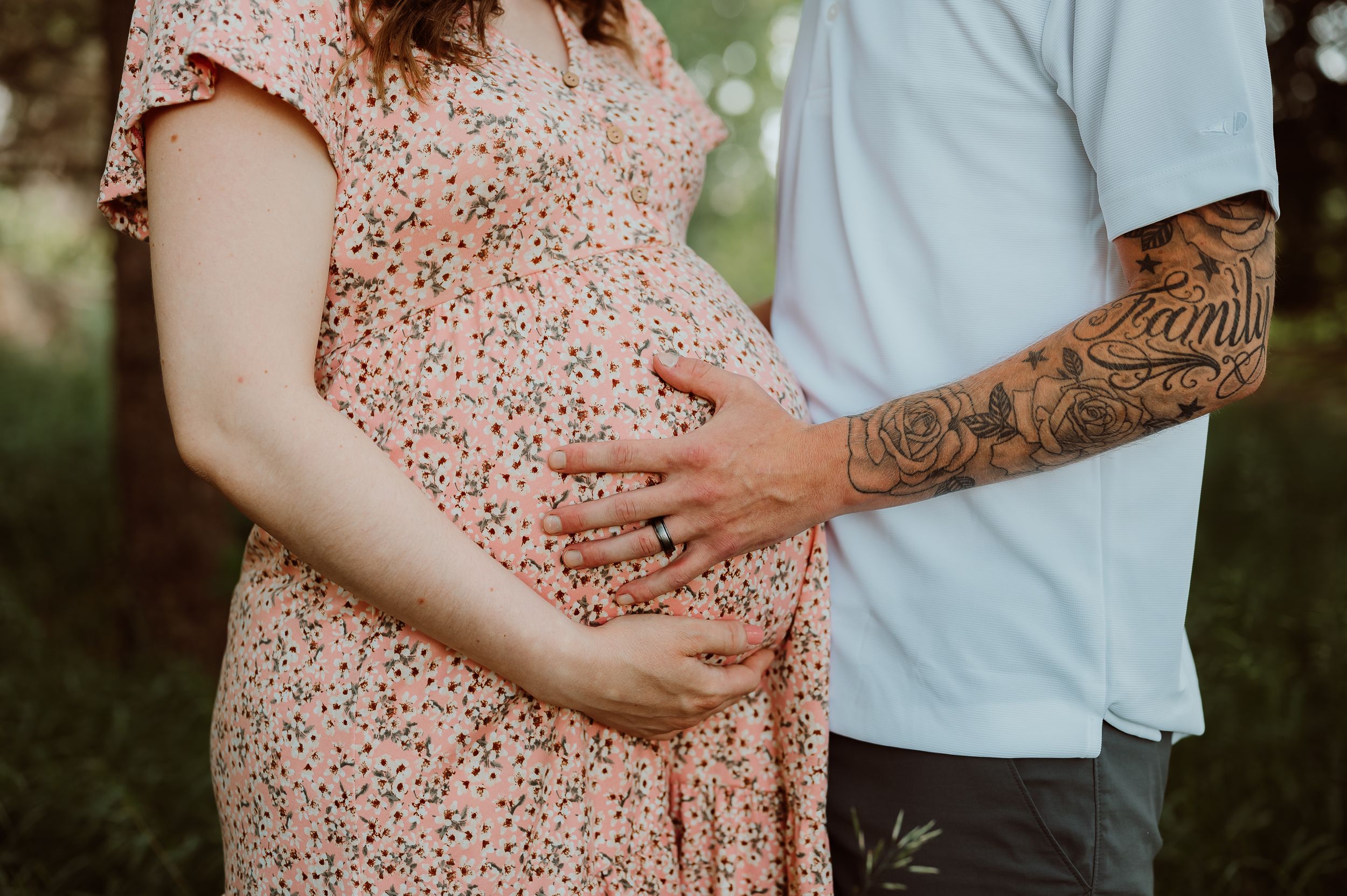 Maternity photoshoot featuring a floral dress and gentle embrace in a natural outdoor setting.