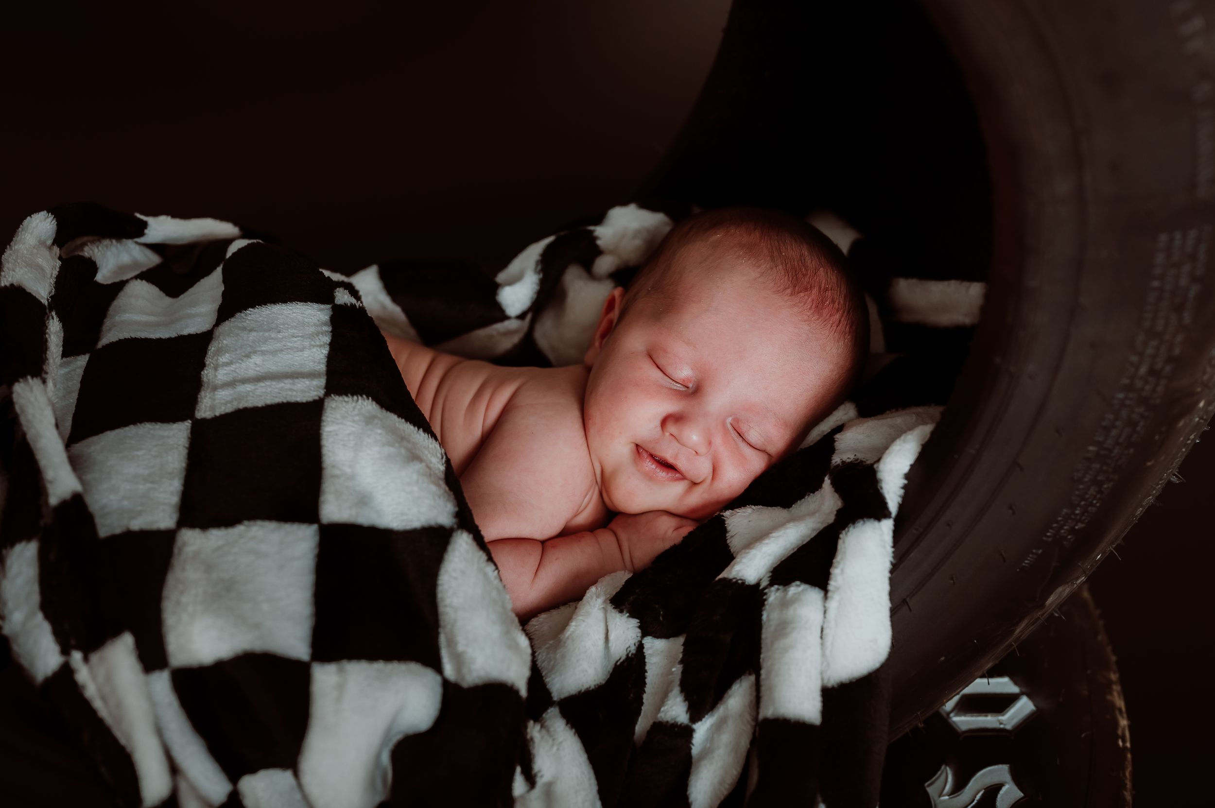 A sleeping newborn baby wrapped in a black and white checkered blanket.