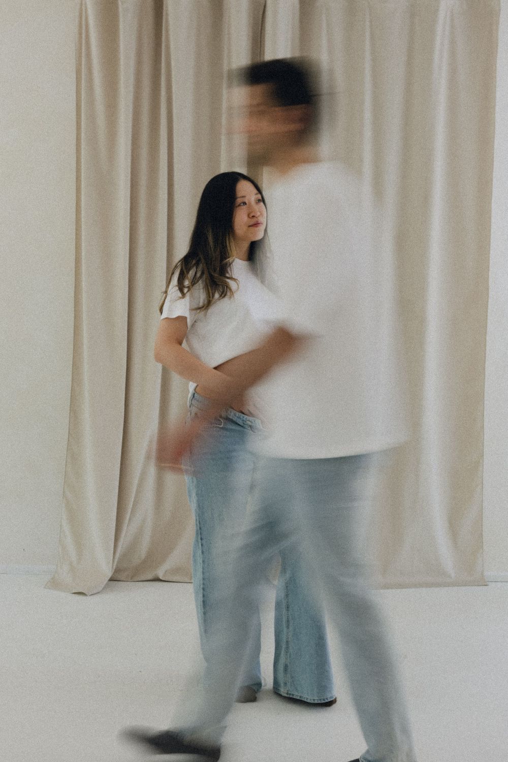 Artistic portrait of two people in casual white tops and light denim against a curtained backdrop with motion blur effect.