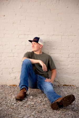 Senior boy pose sitting while leaning against a brick wall