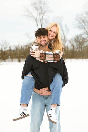 Young couple enjoying a snowy winter day, man giving woman a piggyback ride outdoors.