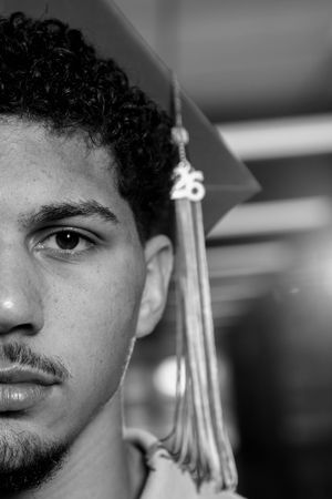 Black and white portrait of a young man wearing a graduation cap with a 26 tassel, close-up half-face shot.