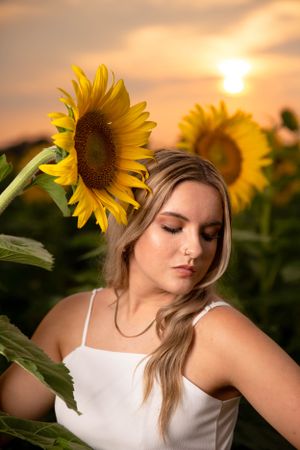 Senior girl pose holding sunflower in sunflower field at sunset