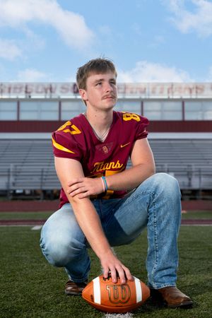 High school football player in Titans jersey crouching on field with football during senior portrait photo session.