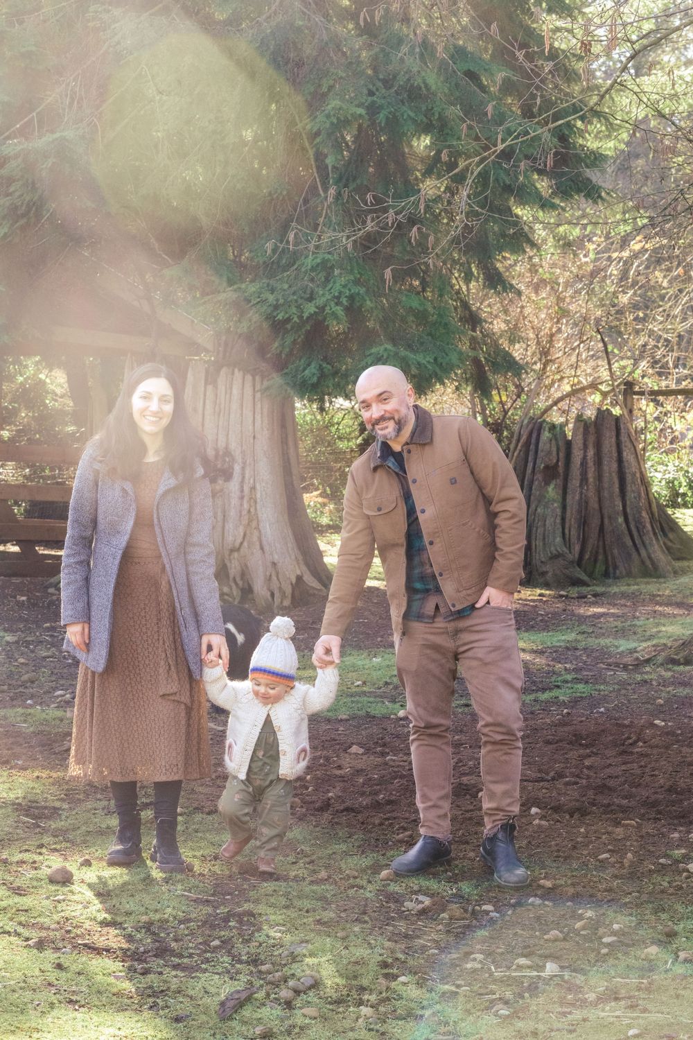 Parents walking their toddler between them through sunlit cedar woods at Enchanted Farms in Duvall, WA.