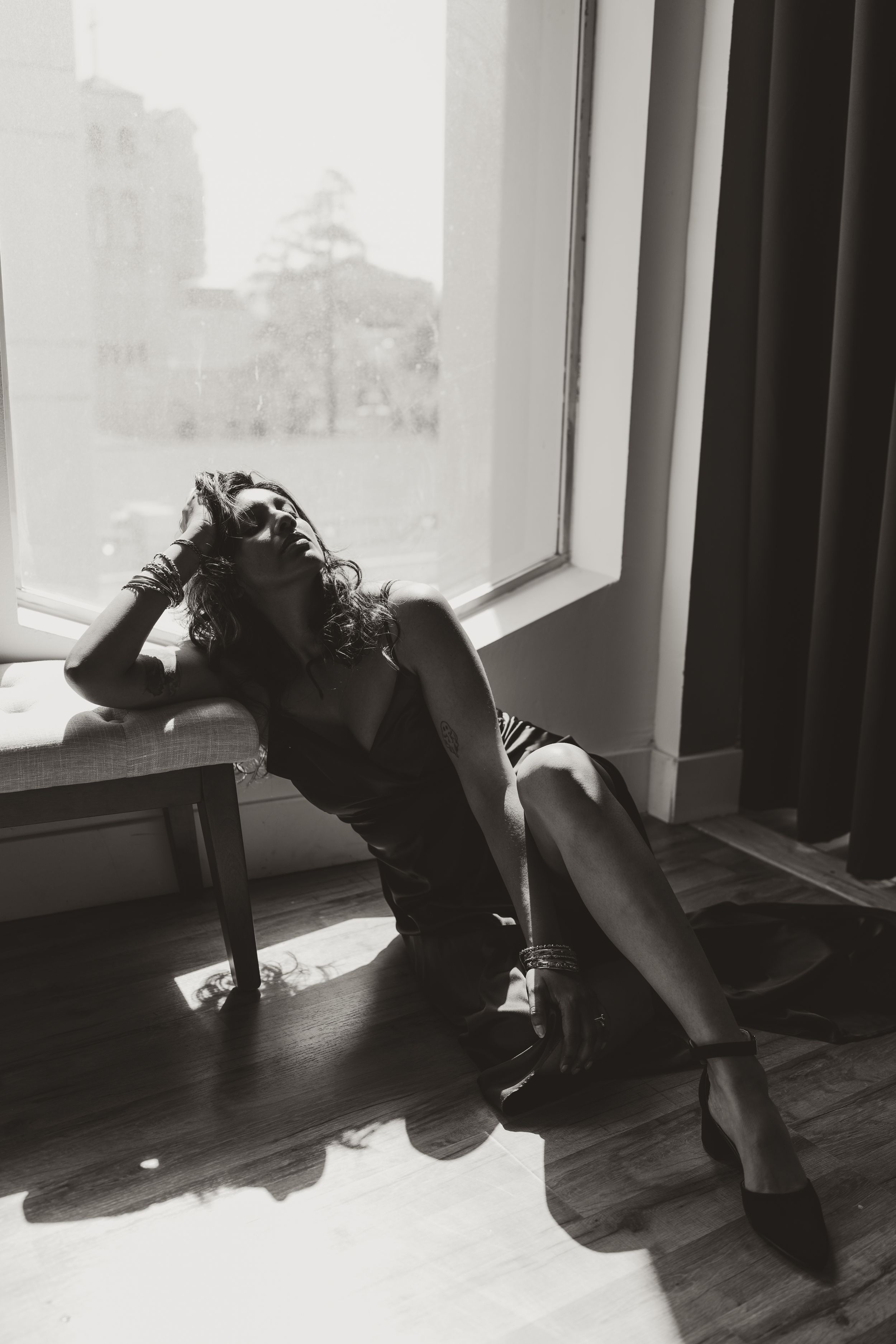 Black and white photo showing a silhouetted figure in a flowing dress lounging gracefully near a window.