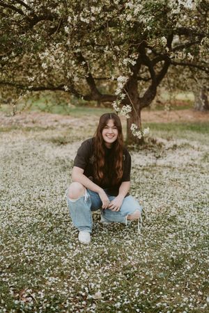Someone crouches in a field of grass under a blooming tree on a summer day.